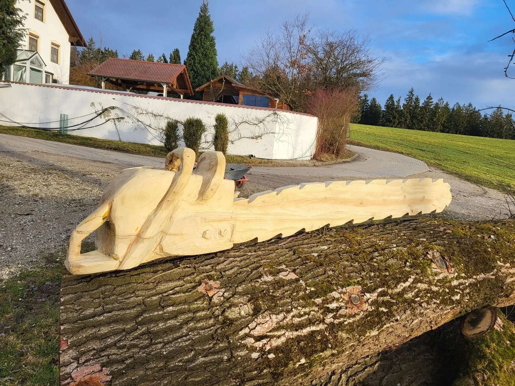 Überlebensgroße Motorsäge aus Holz geschnitzt, liegend auf einem Baumstamm