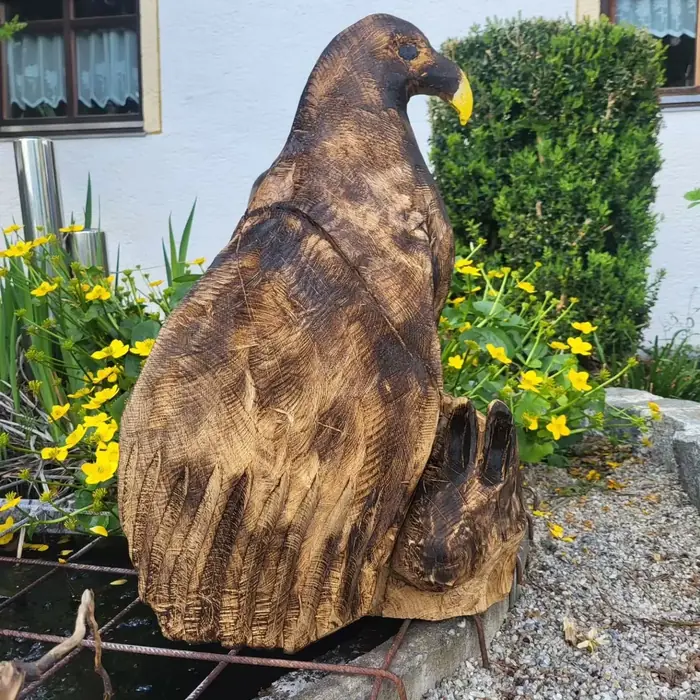 Dunkel gebrannte Adlerskulptur aus Holz zwischen blühenden Stauden