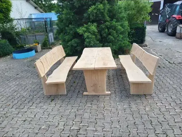 Gartengarnitur aus hellem Holz mit Tisch und zwei Bänken auf gepflastertem Hof