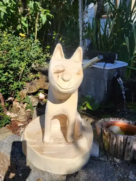 Sitzende Katzenskulptur aus hellem Holz im Garten